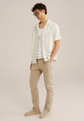 Kurzärmliges cremerfarbenes Hemd mit braunem Blumenmuster, weißes Tanktop, hellbraune Slim-Fit-Hose und beiges Slipper. Stylishe Sonnenbrille rundet den Look ab.