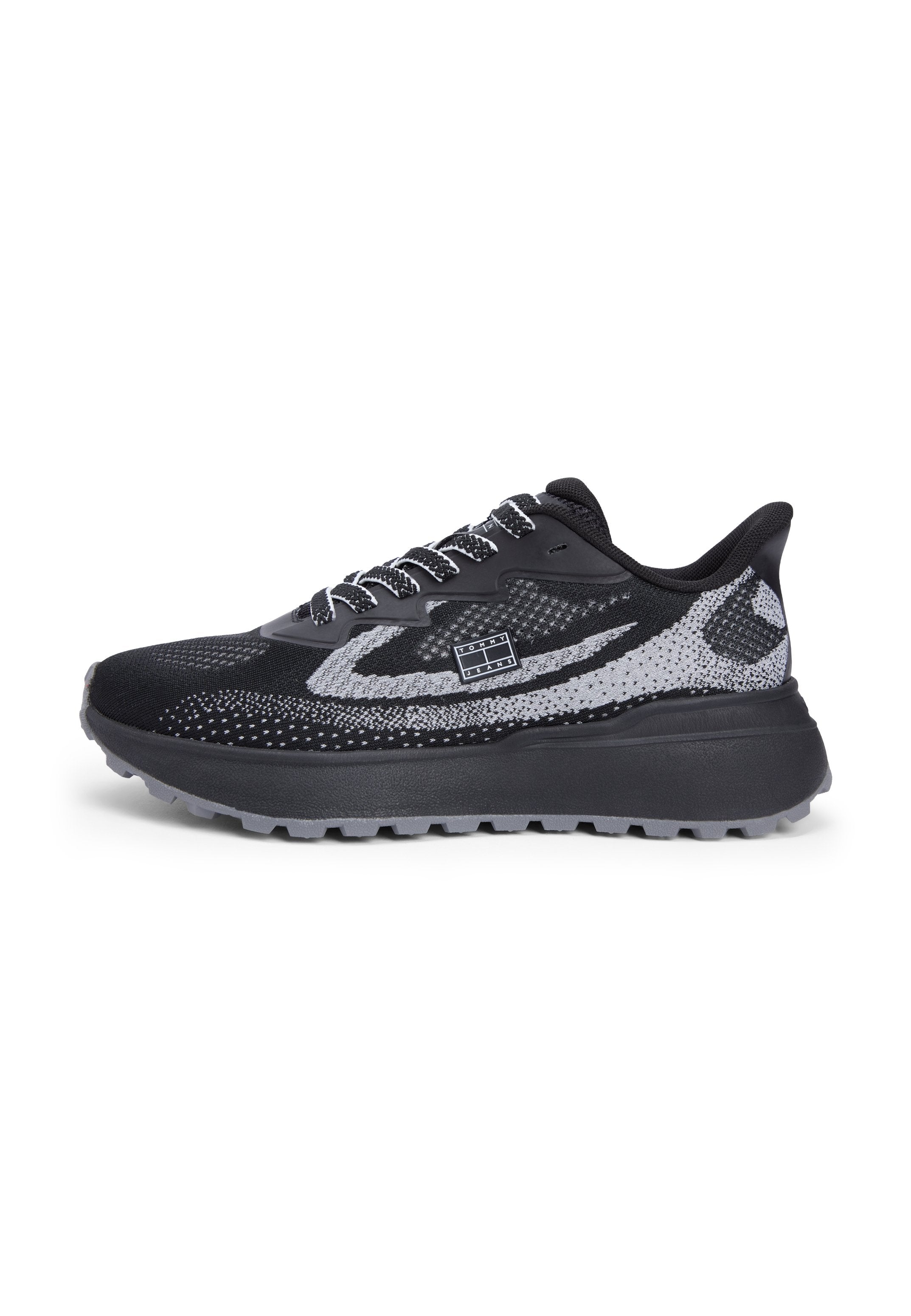 Schwarzer und grauer Strick-Sneaker mit weiß gesprenkeltem Muster, schwarzer Sohle, Schnürverschluss und kleinem rechteckigem Logo an der Seite.