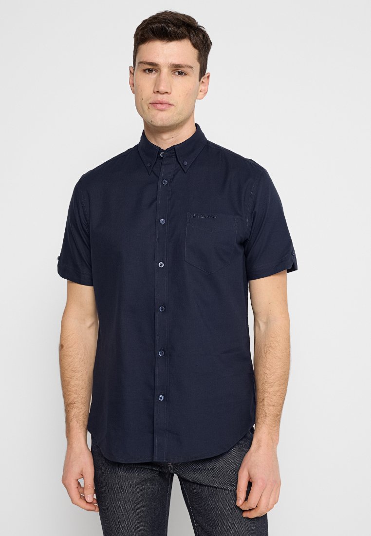 Kurzes, navy-blaues Hemd mit Knöpfen aus Baumwollmischung, ausgestattet mit einer Brusttasche und subtilen Stickdetails für einen sauberen, modernen Look.