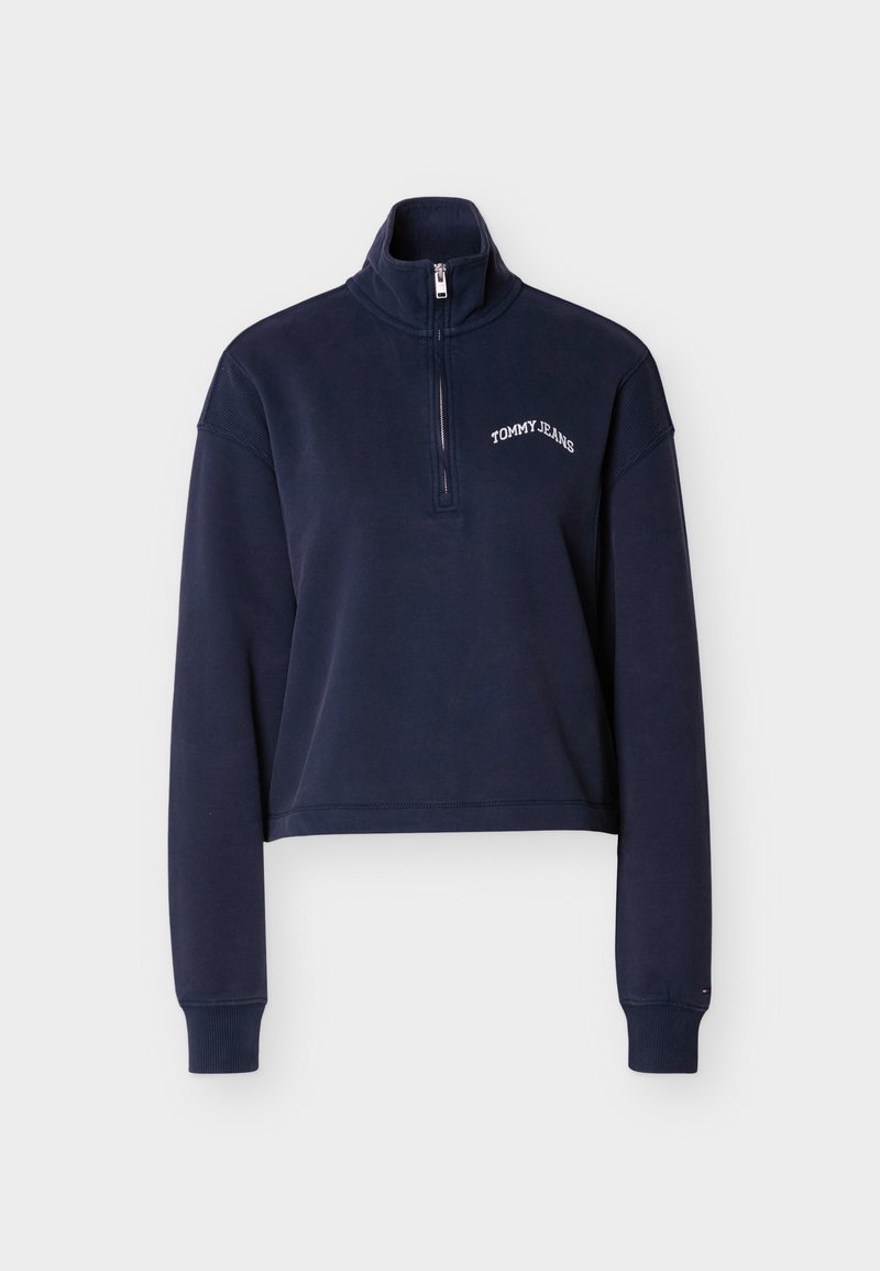 Marineblaues, kurzes Sweatshirt mit hohem Kragen, halbem Reißverschluss und weißem "TOMMY JEANS"-Logo. Weicher Stoff und gerippte Bündchen.