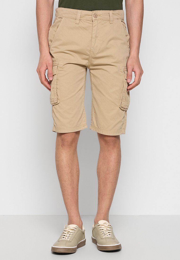 Beige Cargo-Shorts aus leichtem Material, mit seitlichen Taschen und geradem Bein. Getragen mit hellen Sneakers.