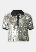 Gekürztes Poloshirt mit silbernen Pailletten, schwarzem Kragen und Knopfleiste. Kurze Ärmel und strukturierte Oberfläche mit schimmerndem Effekt.