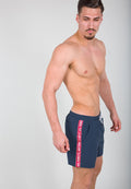 Marineblaue Schwimmshorts mit elastischem Bund und Kordelzug, ausgestattet mit einem roten Seitenstreifen, auf dem "REMOVE BEFORE FLIGHT" steht.