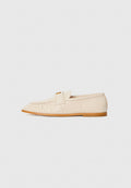 Helle beige Lederloafers mit runder Zehenform, gefälteltem Detail und einem goldenen Akzent an einem Riemen. Flache Sohle mit glatter Textur.