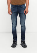 Mann in schmal geschnittenen blauen Jeans und schwarzen Sneakers, der vor einem schlichten weißen Hintergrund steht.