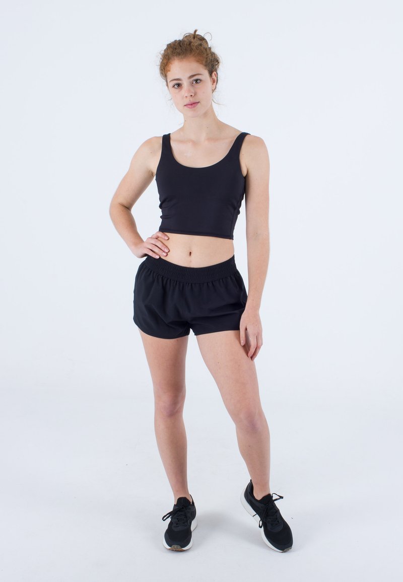 Schwarzes, athletisches Croptop und Shorts aus elastischem Stoff, mit einer taillierten Passform und hohem Bund, kombiniert mit schwarzen Sportschuhen.