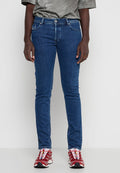 Person trägt eine Slim-Fit blaue Jeans, graues Shirt und rot-weiße Sneakers, steht vor einem schlichten hellgrauen Hintergrund.