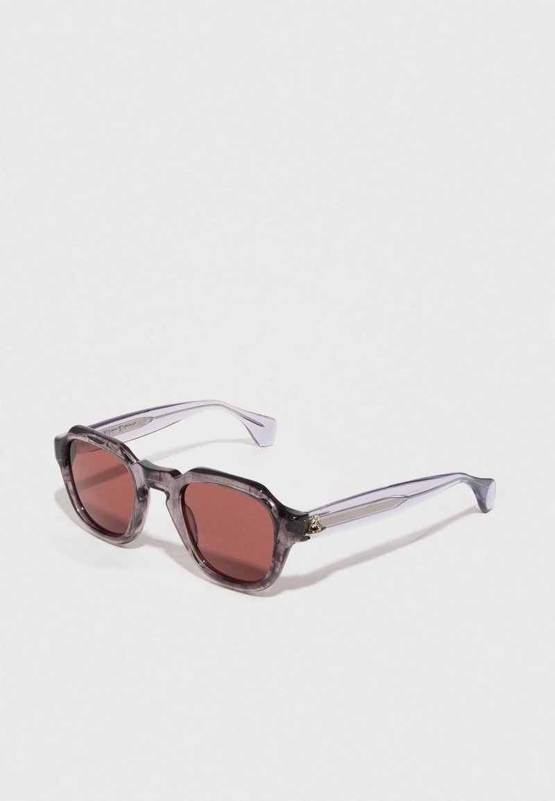 Lila getönte Sonnenbrille mit einem klobigen, transparenten Rahmen. Die Gläser sind dunkelrot. Verfügt über gebogene Bügel und subtile goldene Akzentdetails.