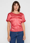 Rosafarbene Satinbluse mit kurzen Ärmeln, Rundhalsausschnitt und gerafften Details. Kombiniert mit hochgeschnittenen Jeans aus Denim, insgesamt glatte Textur.