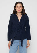 Marineblaue Wickeljacke mit großem Kragen, tailliertem Gürtel und langen Ärmeln, aus weichem Material gefertigt. Kombiniert mit hellen Jeans.