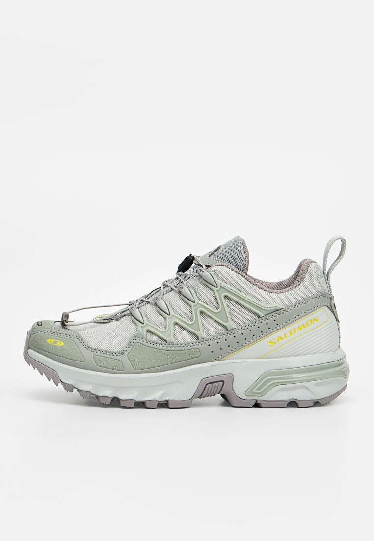 Hellgrauer und weißer Trailrunning-Schuh mit strukturierter Sohle, Schnellverschluss-System und gelbem Salomon-Logo an der Seite.