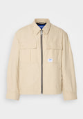 Beige Jacke mit einem Frontreißverschluss, zwei Brusttaschen und einem kleinen Markenetikett. Hergestellt aus einem glatten, leichten Stoff.
