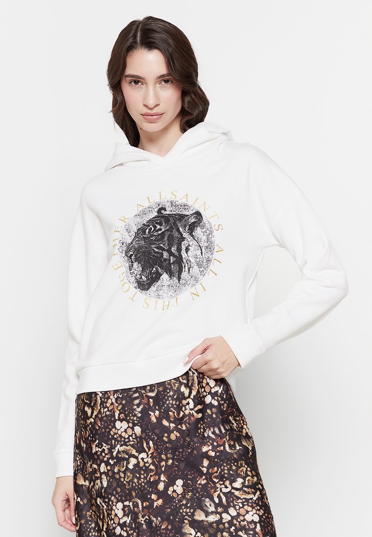 Frau in einem weißen Hoodie mit einem brüllenden Tiger-Print und Text, kombiniert mit einem Rock in braunen und schwarzen abstrakten Mustern.
