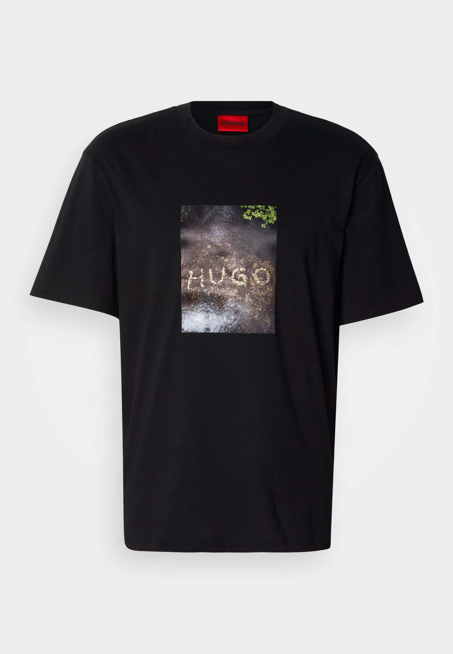 Schwarzes Baumwoll-T-Shirt mit einem rechteckigen Grafikdruck, der das Wort "HUGO" auf einer strukturierten Oberfläche zeigt. Kurze Ärmel, Rundhalsausschnitt.