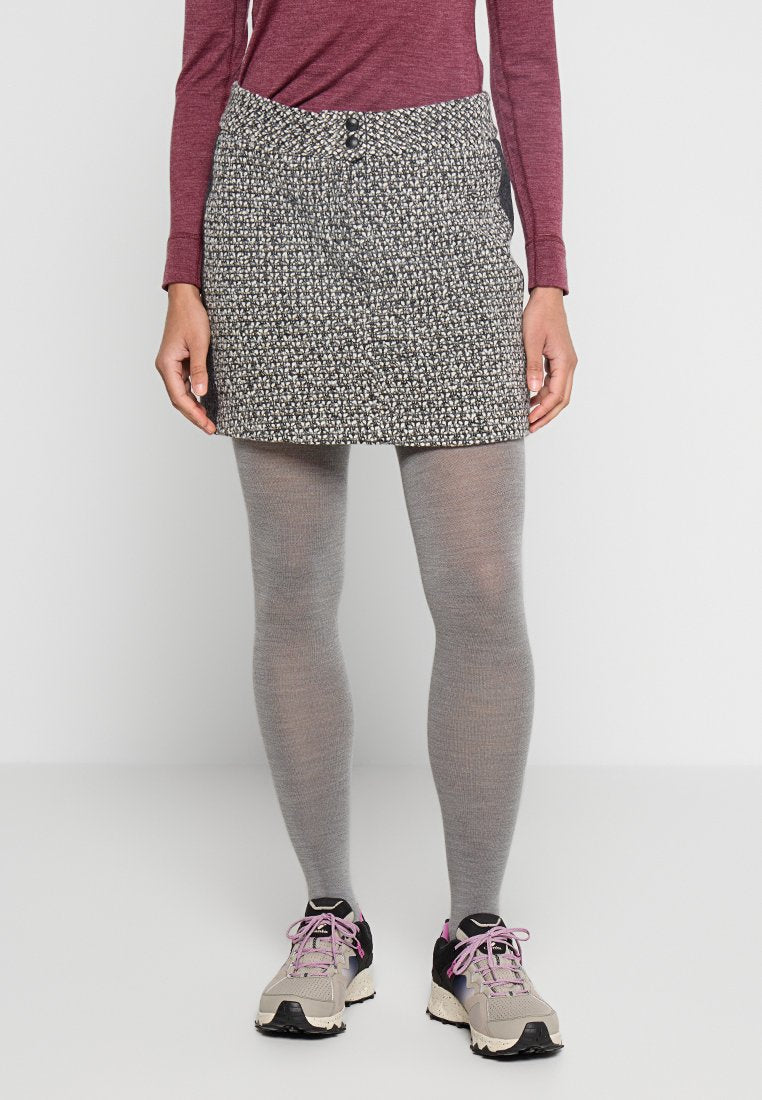 Strickrock mit einem strukturierten Schwarz-Weiß-Muster, mit einem Bund mit zwei Knöpfen. Kombiniert mit grauen Strumpfhosen und leichten Sneakers.