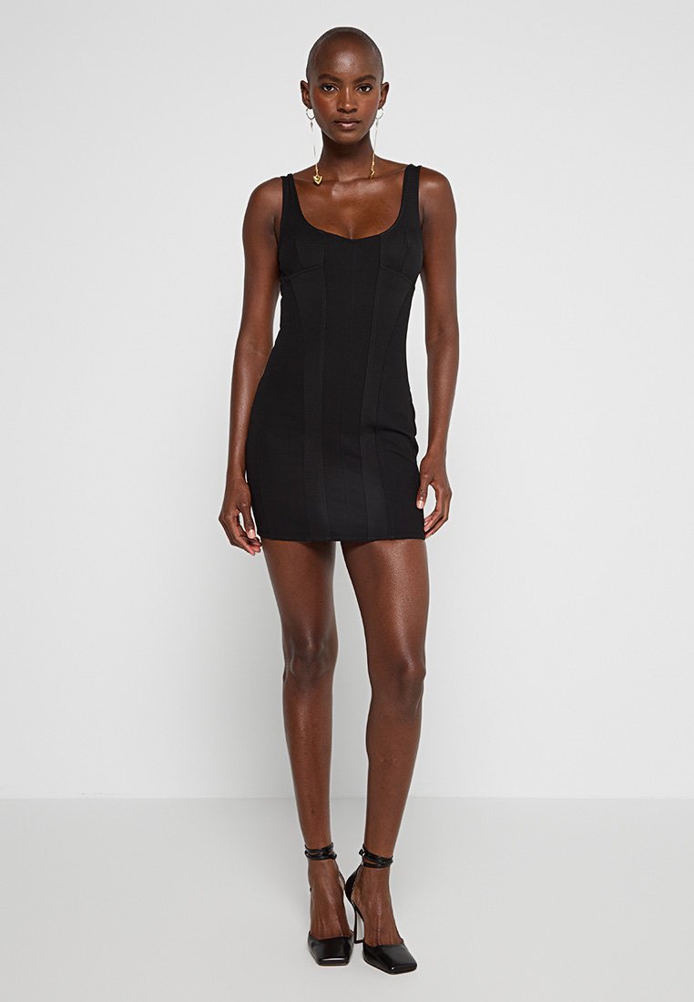 Schwarzes Bodycon-Kleid mit Rundhalsausschnitt und dünnen Trägern. Verfügt über vertikale Nahtdetails und eine figurbetonte Silhouette. Kombiniert mit schwarzen High Heels.