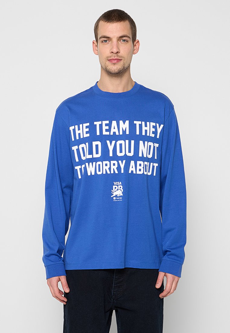 Blaues langärmeliges T-Shirt aus Baumwolle mit großem weißen Text auf der Vorderseite. Der Text lautet: "THE TEAM THEY TOLD YOU NOT T'WORRY ABOUT."