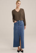 Braunfarbenes Langarmoberteil mit Spitzenbesatz, kombiniert mit einem hellblauen Jeans-Maxikleid mit einem Schlitz vorne und Taschen. Schwarze spitze Ballerinas.