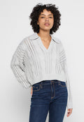 Hellgrauer, verkürzter Pullover mit V-Ausschnitt und Kragen, ausgestattet mit Zopfmuster und offenen Strickdetails. Kombiniert mit dunklen Jeans.