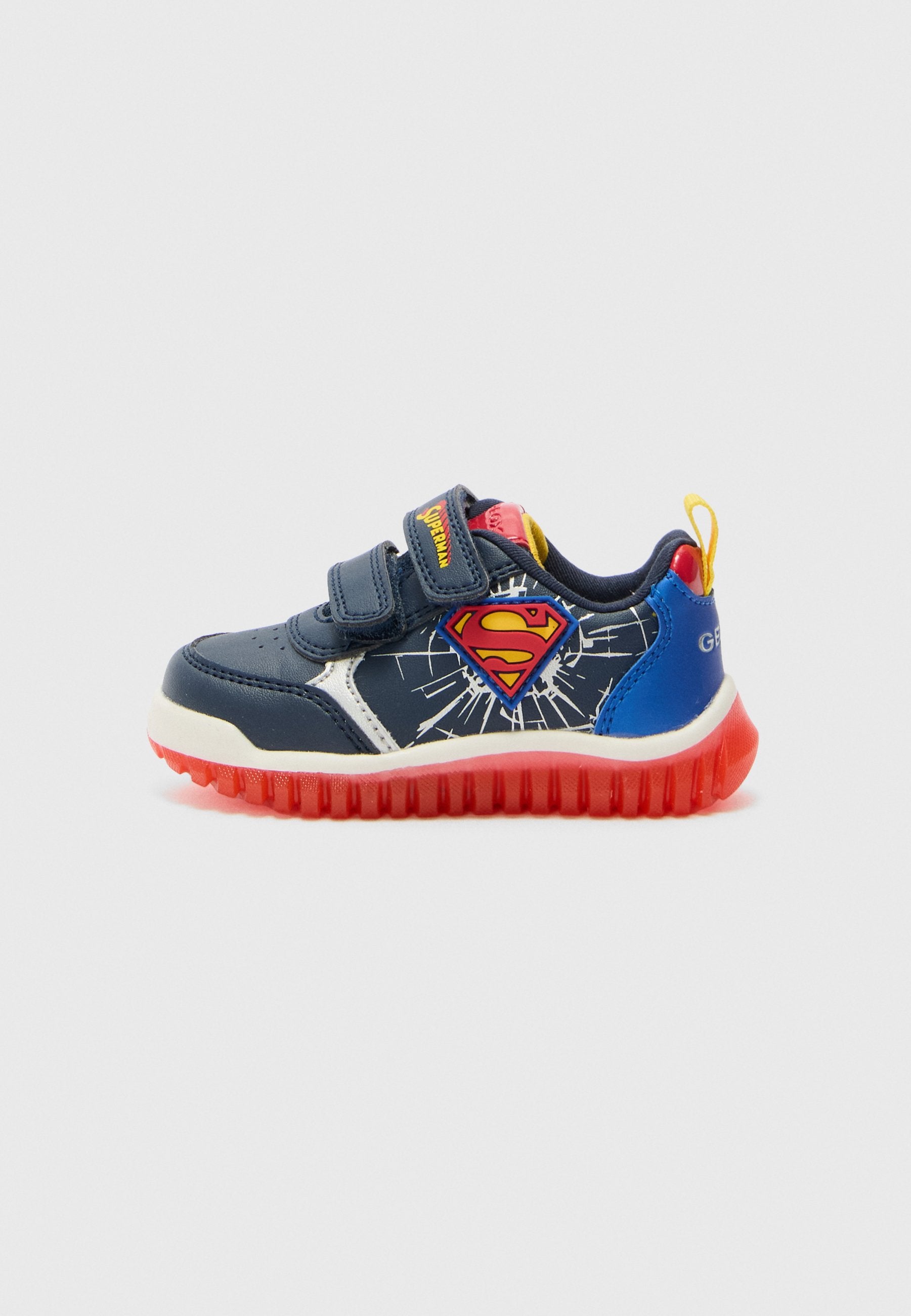 Marineblaue Kindersneaker mit roter Sohle, weißen Akzenten, Klettverschlüssen und einem Superman-Logo an der Seite, das ein Ausbruchdesign zeigt.
