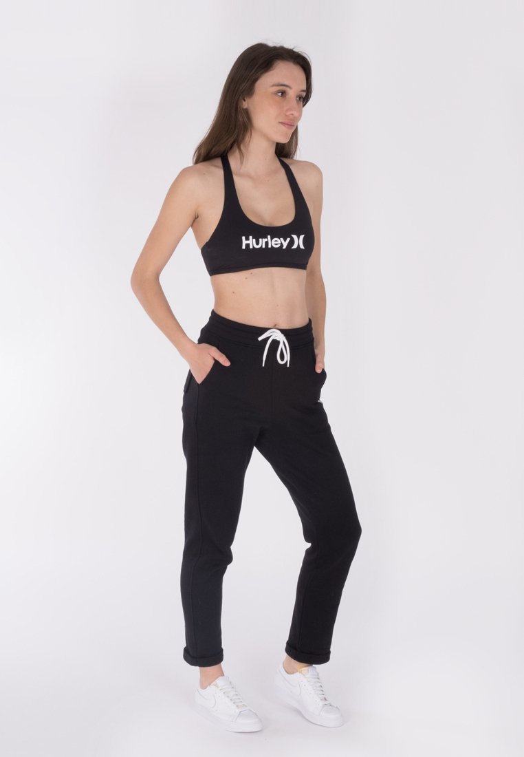 Schwarzer Sport-BH mit "Hurley"-Logo, kombiniert mit schwarzen, schmal zulaufenden Jogginghosen mit elastischem Bund und Kordelzug, getragen mit weißen Sneakers.