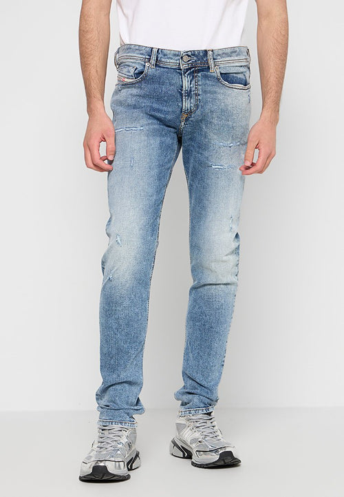 Mann in verblassten, blauen, lässigen Slim-Fit-Jeans und silbernen Sportschuhen, stehend vor weißem Hintergrund.