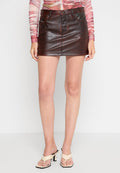 Brauner Kunstleder-Minikilt mit tailliertem Design, Fronttaschen und einem dezenten Glanz. Getragen mit hellen, geschnürten Absätzen.