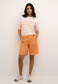 Weißes Hemd mit orangen Streifen, kombiniert mit orangefarbenen Shorts mit Taschen und geradem Schnitt. Getragen mit hellen Sneakern.