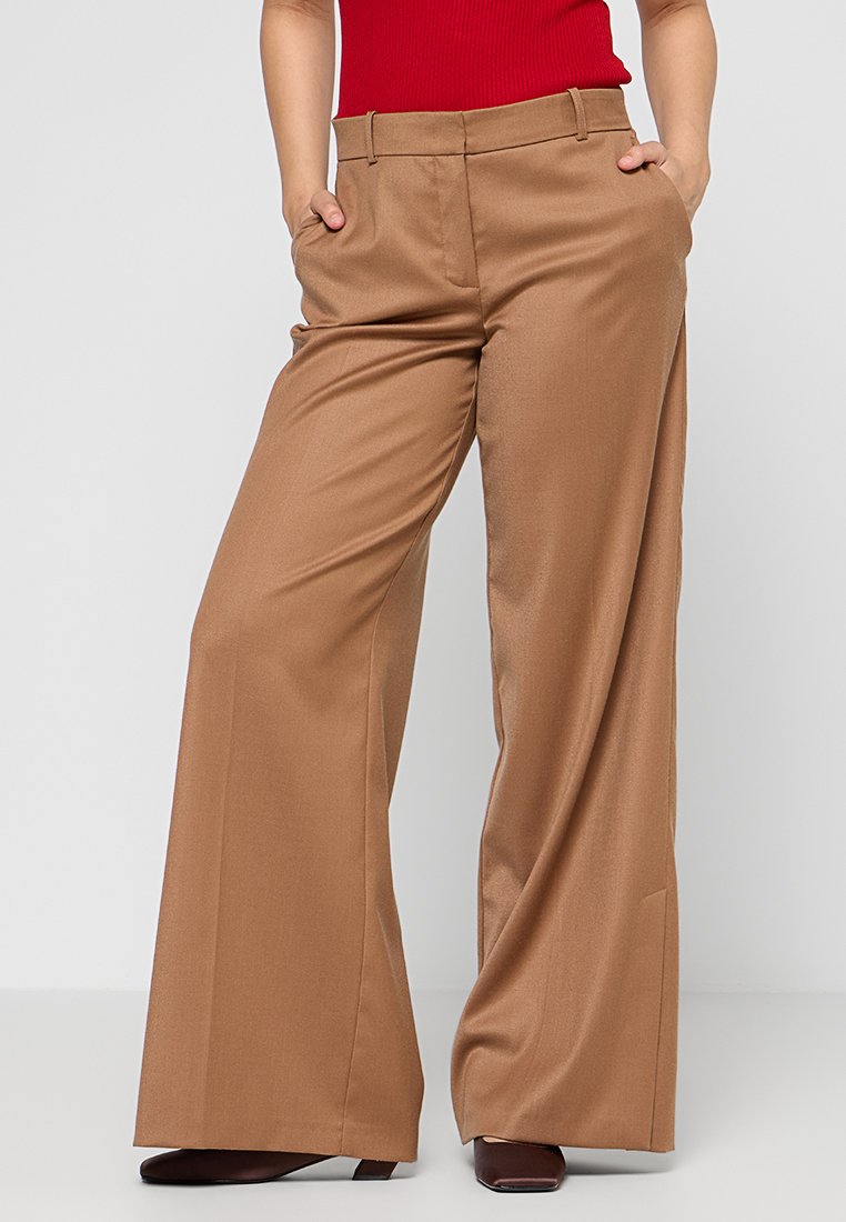 Braune weite Hosen aus glattem Stoff mit einer mittelhohen Taille, Vorderaschen und einem taillierten Schnitt. Kombiniert mit einem roten Oberteil.