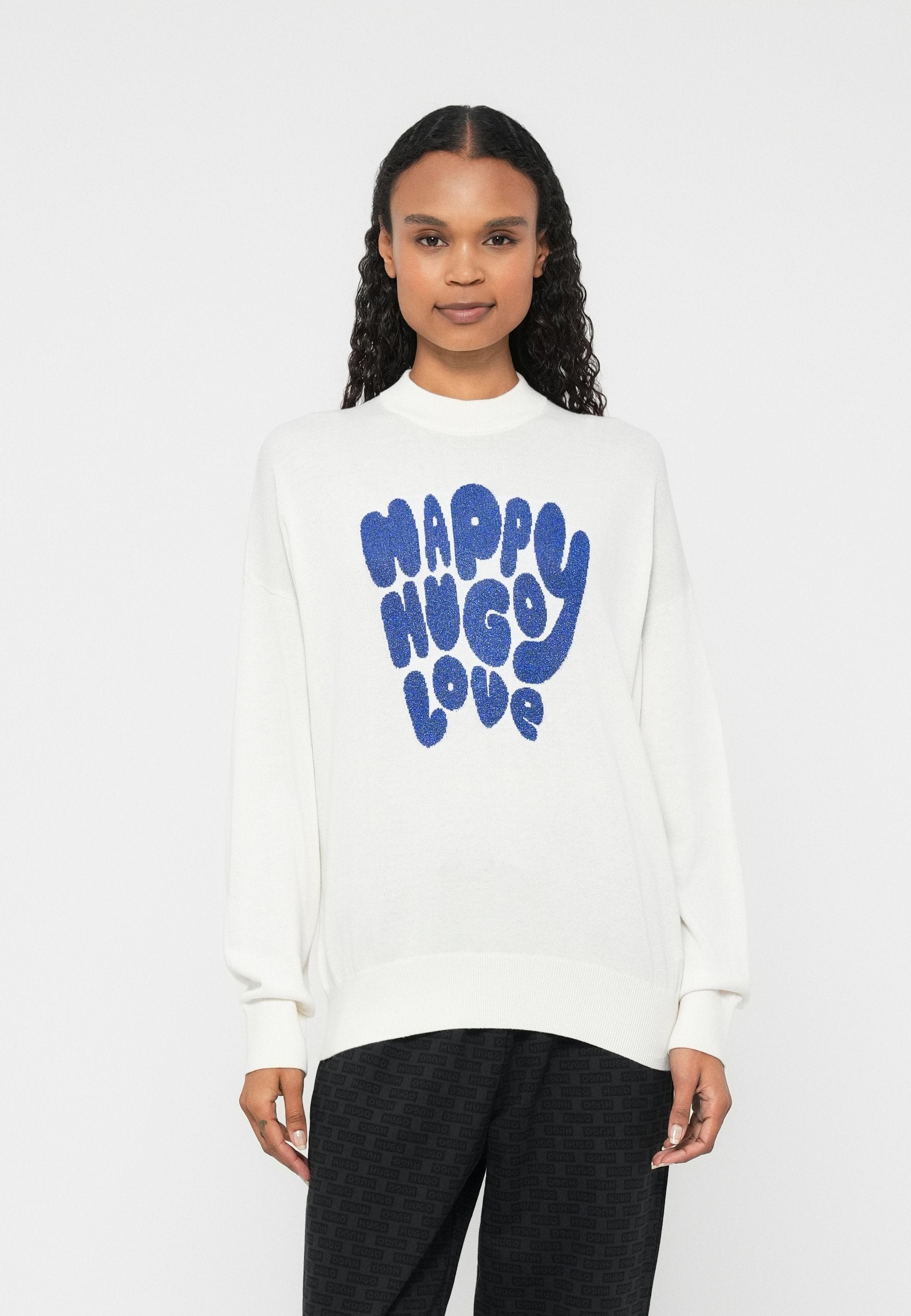 Weißer Pullover mit hohem Kragen und langen Ärmeln, auf der Vorderseite mittig blaue, flauschige Schrift mit dem Text "HAPPY HUGO LOVE".