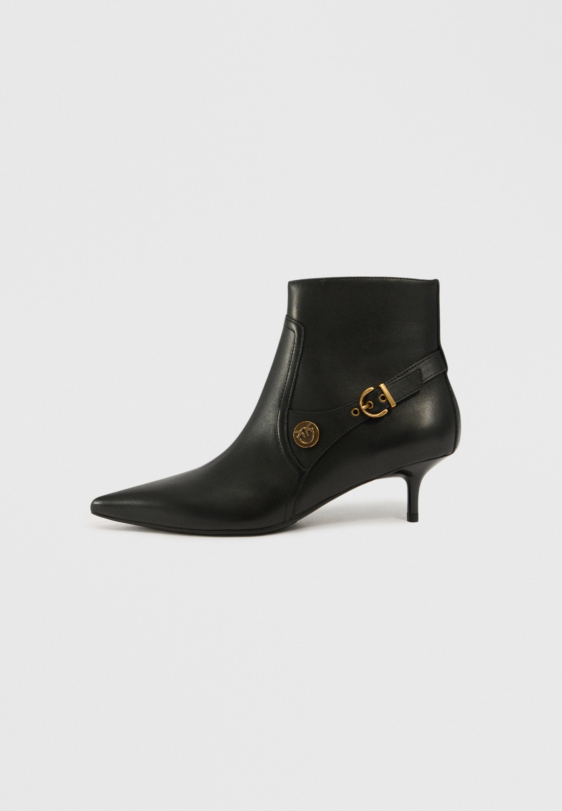 Schwarze Leder-Ankle-Boots mit spitzer Zehenform, niedrigem Absatz und goldenen Hardware-Details, die ein kreisförmiges Akzentstück und einen seitlichen Riemen aufweisen. Glatte Textur.