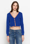 Gekürzter Cardigan aus lebhaft blauem Rippstoff mit orangefarbenen Akzenten und Knöpfen, ausgestattet mit einem V-Ausschnitt und langen Ärmeln. Kombiniert mit blauen Jeans.