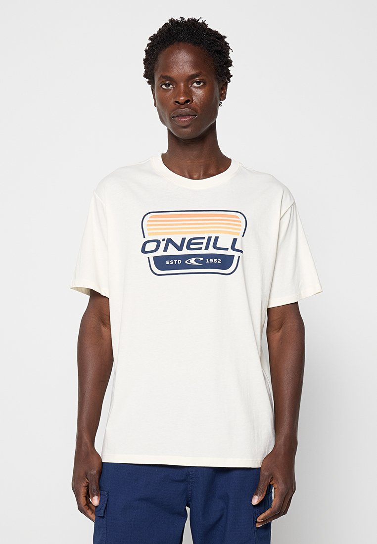 Person trägt ein weißes O'Neill-T-Shirt mit orange-blauen Streifen, kombiniert mit dunkelblauer Hose, vor einem einfarbigen Hintergrund stehend.