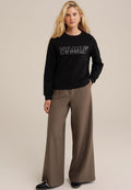 Schwarzer Sweatshirt mit den fettgedruckten Buchstaben "SYDNEY", kombiniert mit beigen, weitem Hosen. Das Material wirkt weich, mit einem entspannten Schnitt und Rundhalsausschnitt.