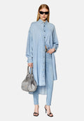 Frau in einem übergroßen hellblauen Denim-Hemd, passender Jeans, schwarzen Sonnenbrille, schwarzen Absatzsandalen und mit einer strukturierten grauen Handtasche in der Hand.