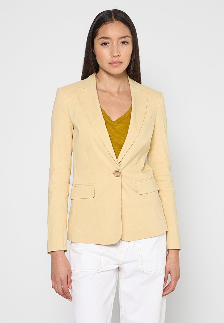 Hellgelbes tailliertes Blazer mit langen Ärmeln, Ein-Knopf-Verschluss, zwei Vorderaschen und einer glatten Stofftextur. Getragen über einem senfgelben Oberteil.