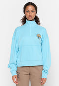 Hellblaues Pullover-Sweatshirt mit hohem Kragen, halblanger Reißverschlussöffnung und einem Emblem von Wellen und Sonne auf der linken Brust. Weiche Textur.
