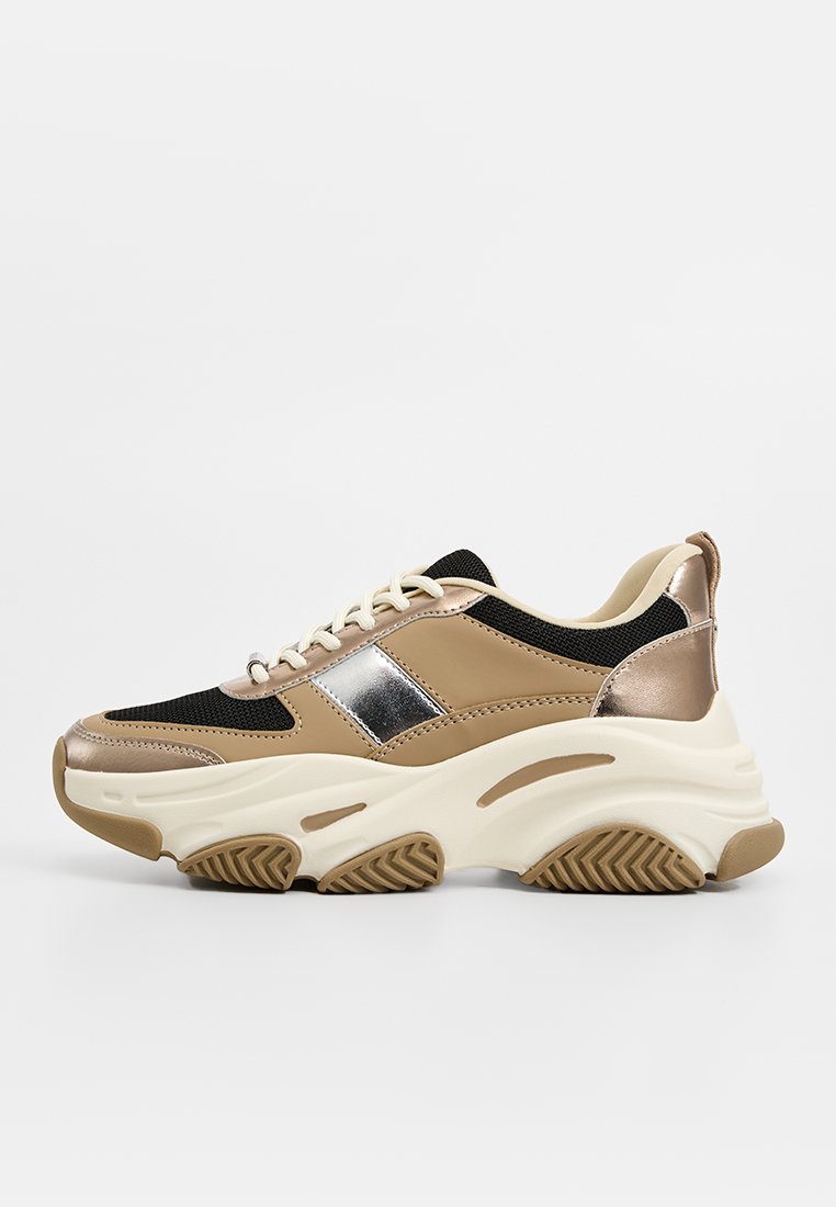 Chunky Sneaker mit einem Obermaterial aus beigem und schwarzem Netz, metallischen silbernen Akzenten und einer dicken, strukturierten weißen Sohle. Mit abgerundetem Zehenbereich und Schnürung.