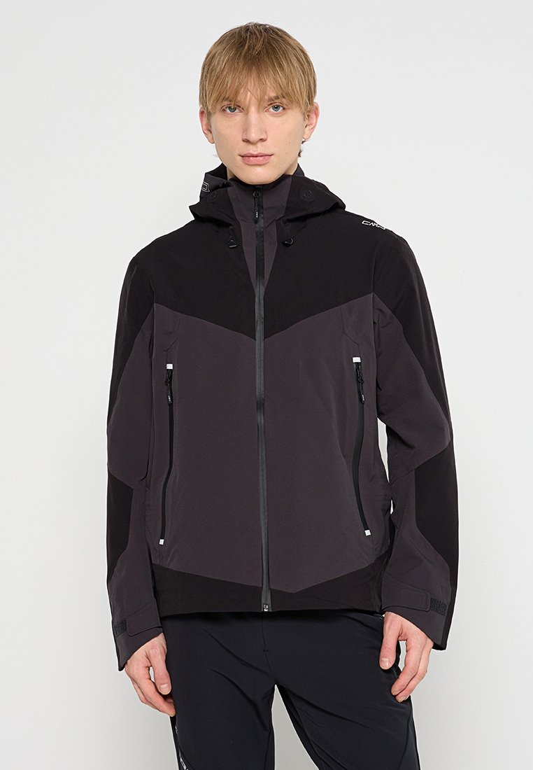 Männliche schwarze und dunkelgraue Softshell-Jacke mit Reißverschluss vorne, verstellbare Kapuze und seitlichen Reißverschlusstaschen. Merkmale ein Farbblockdesign.