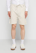 Mann trägt beige und weiß vertikal gestreifte Shorts mit Kordelzug, weiße Socken, weiße Sneaker und ein weißes langärmeliges Hemd und steht.