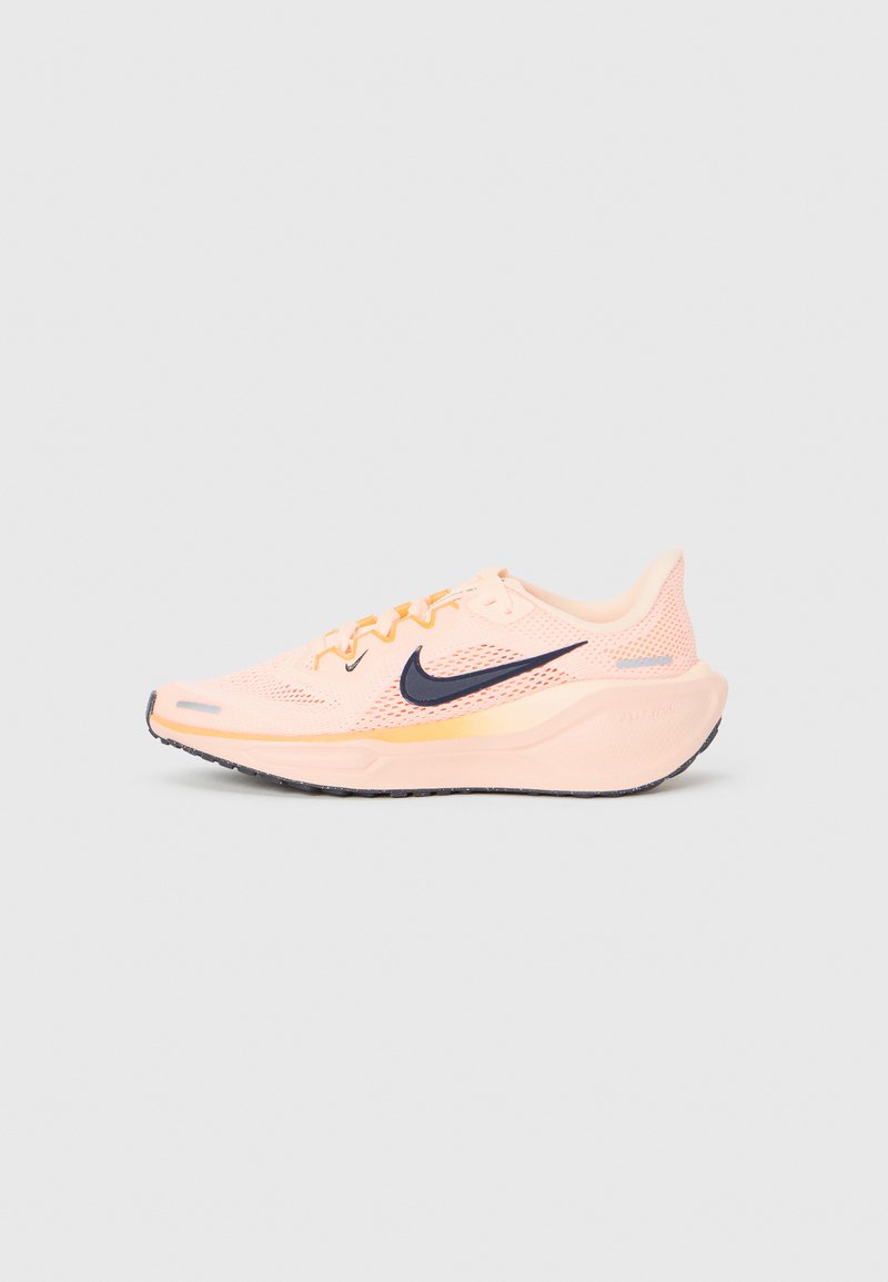 Hellrosa Nike Laufschuh mit schwarzem Swoosh-Logo, Mesh-Obermaterial und dicker gepolsterter Sohle, von der Seite vor einem schlichten Hintergrund abgebildet.