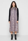 Leopardenmuster-Kleid mit hohem Ausschnitt und kurzen Ärmeln, aus fließendem Stoff mit einem schwarzen Strickakzent an den Armen. Schwarze Stiefeletten.