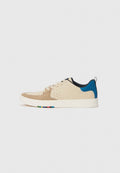 Beige Wildleder- und Leder-Sneaker mit einer blauen Fersenlasche, perforierten Akzenten und bunten Details auf der Sohle. Flache Schnürsenkel und Gummisohle.