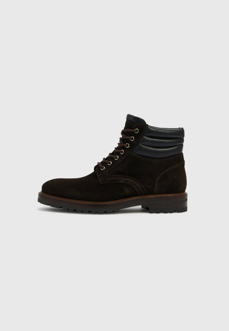 Dunkelbrauner Veloursleder-Schnürstiefel mit gepolstertem schwarzem Kragen und dicker profillaufsohle, von der Außenseite auf hellem Hintergrund zu sehen.