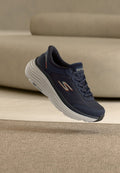 Marineblauer Skechers-Sneaker mit weißer dicker Sohle, entworfen für maximalen Komfort durch Polsterung, platziert auf beigefarbenem Teppich vor Sofahintergrund.