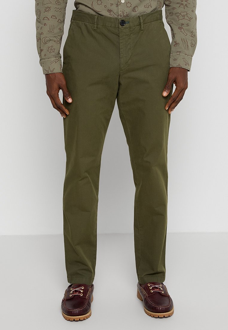 Olivgrüne Chino-Hosen aus leichtem Baumwollstoff. Verfügt über einen Knopfverschluss, Fronttaschen und einen geraden Beinansatz. Getragen mit braunen Schuhen.