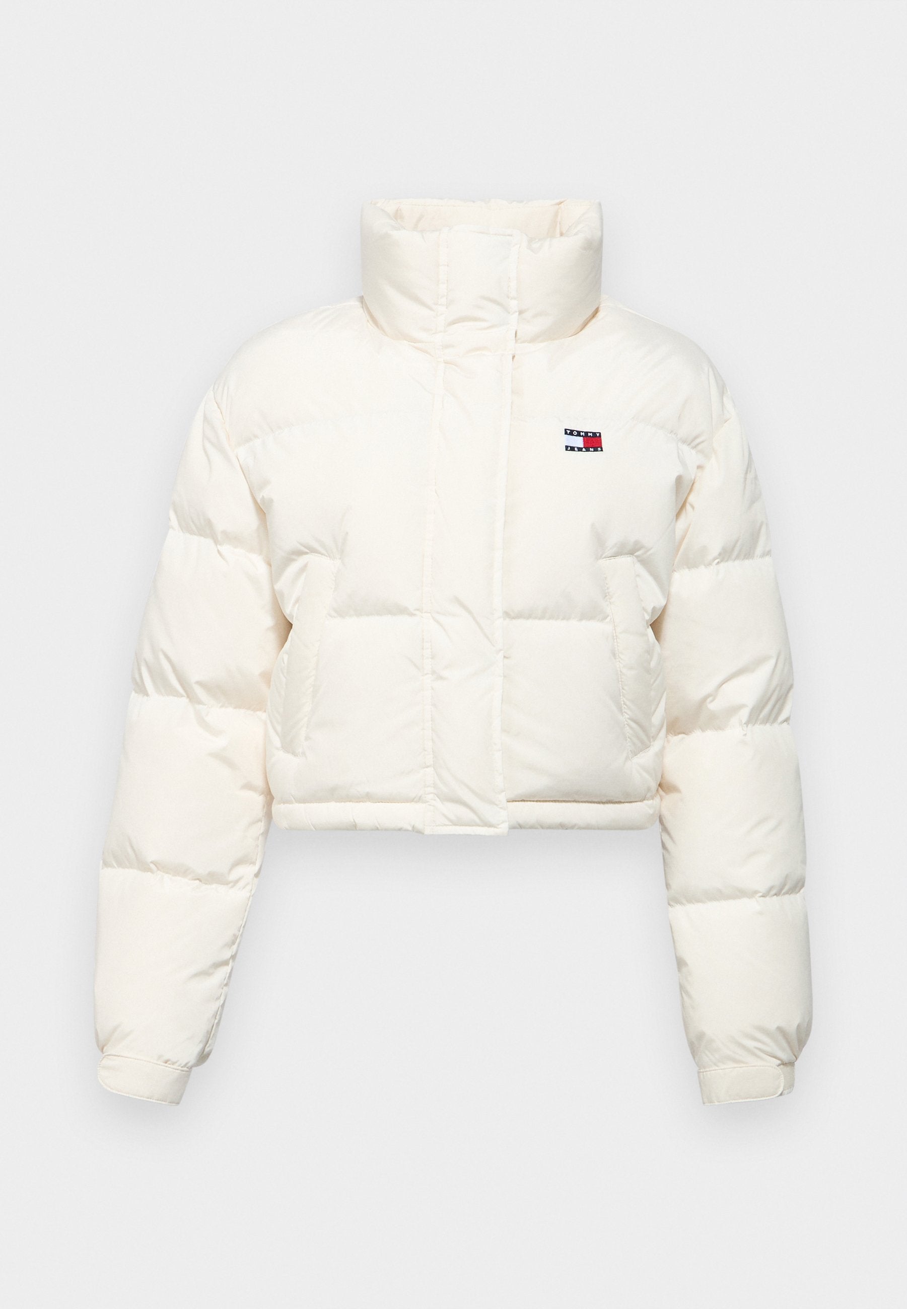 Gekürzte Daunenjacke aus cremefarbenem Stoff mit hohem Kragen, gesteppten Abschnitten und einem kleinen Logodetail auf der Brust. Akzentuierte Bündchen.