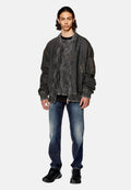 Übergroße graue Denim-Bomberjacke mit gerippten Bündchen, Fronttaschen und einer strukturierten Oberfläche, kombiniert mit blauen, ausgewaschenen Jeans und schwarzen Sneakers.