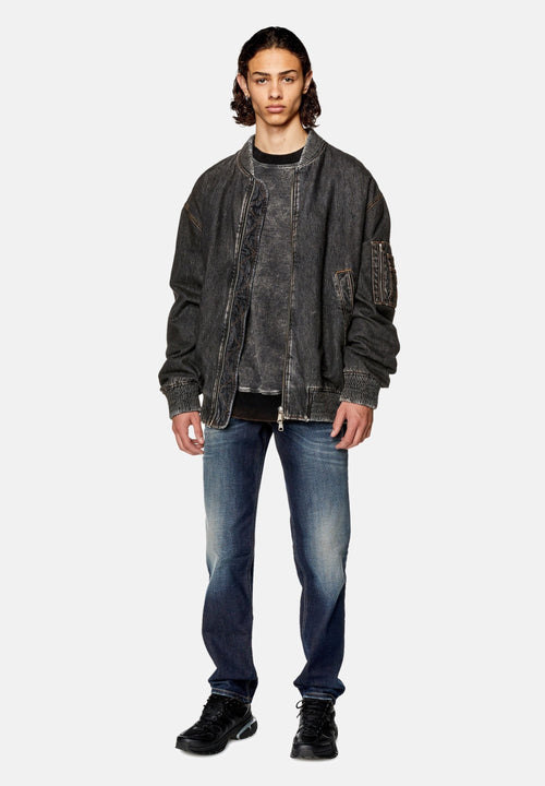 Übergroße graue Denim-Bomberjacke mit gerippten Bündchen, Fronttaschen und einer strukturierten Oberfläche, kombiniert mit blauen, ausgewaschenen Jeans und schwarzen Sneakers.
