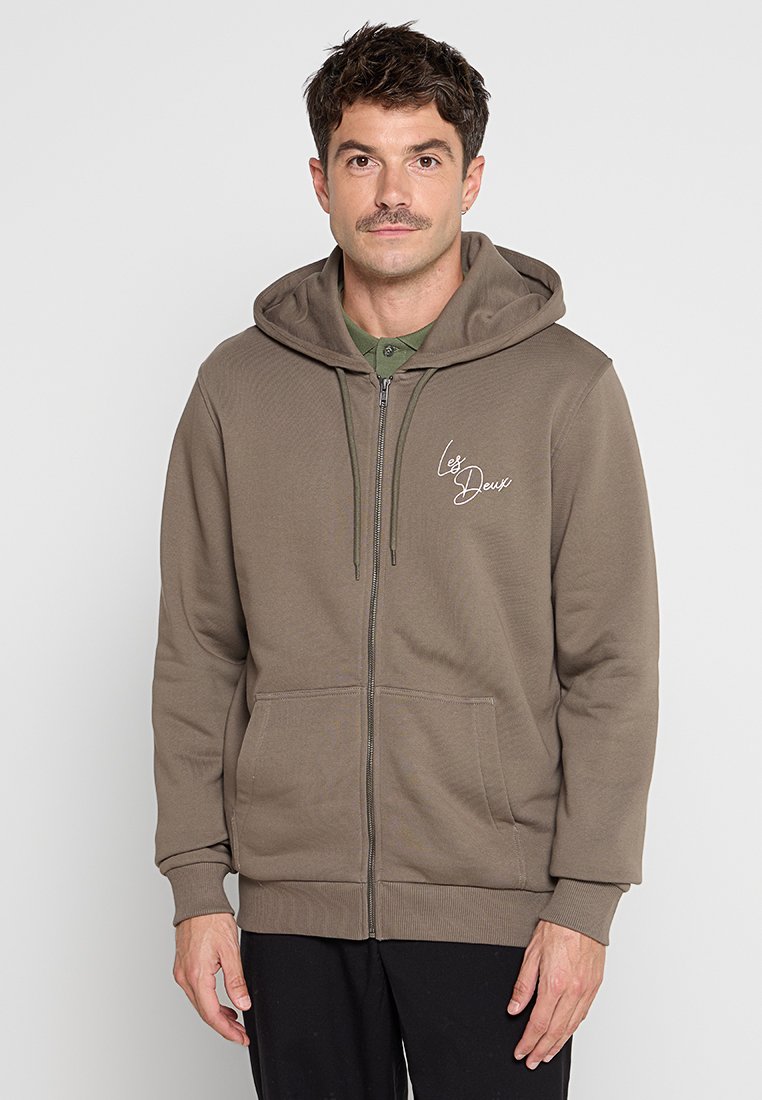Kapuzensweatshirt mit Reißverschluss in Olivgrün, aus weichem Stoff gefertigt, mit einer Kängurutasche und einem gestickten Logo auf der Brust.